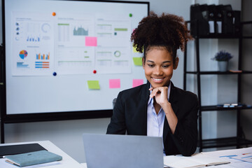 African Businesswoman in suit is working on laptop and calculator for cost with happy face in office space with paperwork.