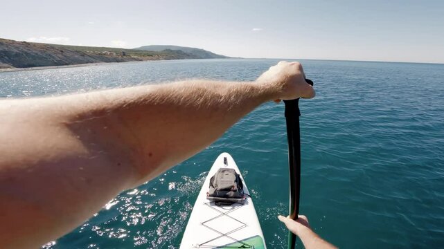 Men rowing on sup board on summer quiet sea. First person view of stand paddle boarding.