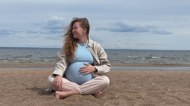 Young happy pregnant woman sitting on the sand on a beach at sea and enjoy nature 