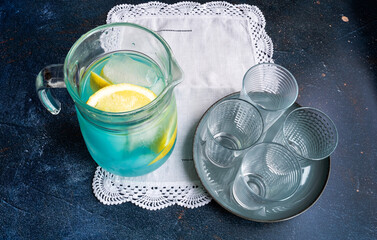 4 vasos de vidrio vacíos sobre un plato de cerámica y una jarra de vidrio con hielo y refresco