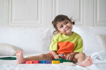 Fototapeta premium Adorable child sitting on a bed with colorful blocks, smiling and enjoying playtime in a bright and cozy room.