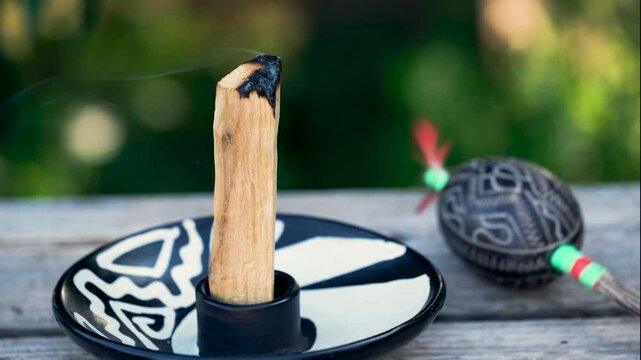 Burning palo santo stick (Bursera graveolens) on a wooden table in the garden in summer