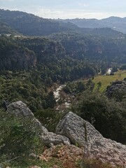 A breathtaking vista of a mountainous landscape featuring dense forests, rugged cliffs, and a winding river cutting through the valley, showcasing nature's raw beauty.