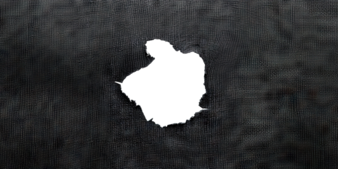 Hole in black fabric with frayed edges, cut out