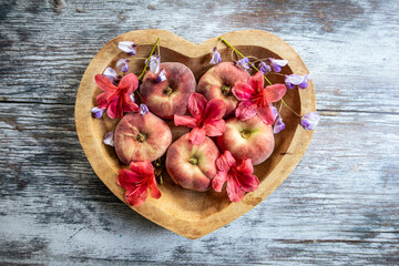 Peaches in a heart shaped wooden dish with fresh flowers