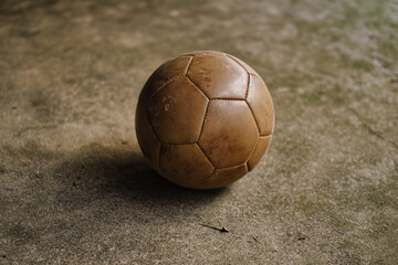 A vintage leather soccer ball, its worn surface and stitching hinting at countless games played. A symbol of global passion and teamwork, bathed in warm morning light.