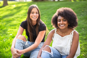 Two beautiful diverse multiracial best friends sitting together and laughing together outdoors on a sunny day. Diversity concept photo of two young women smiling together