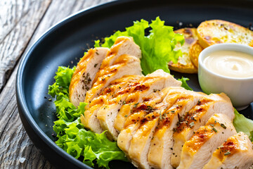 Grilled chicken breast, fried potatoes and fresh vegetables served on black plate on wooden table


