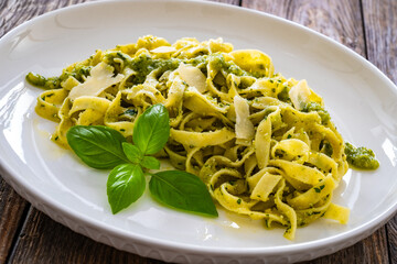 Pappardelle with basil pesto sauce sprinkled with grated Parmesan cheese served on white plate with spoon and fork on wooden table
