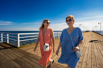 Summer vacation. Two pretty mid-adult women wearing flowing dresses talking and walking on a wooden...
