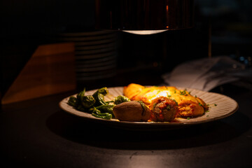 A plate of food with a light shining on it. The plate has a variety of food items including meat, vegetables, and potatoes. The light shining on the plate creates a warm and inviting atmosphere