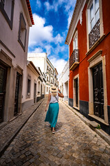 Summer vacation. Beautiful young woman in flowing fashionable clothes and beige hat walking and...