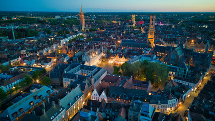 Fototapeta premium Enchanting aerial view of Bruges' historic old town captured by a drone at night! The illuminated medieval architecture, winding canals, and charming cobblestone streets create a magical and captivati