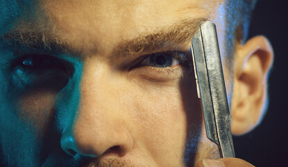 Beard styling. Closeup cropped portrait of brutal man with straight razor near eye. Barbershop advertising. Professional barber with hairdressing tool. Handsome hairdresser ready for shave with razor.