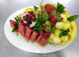 a large white dish with fresh fruits and berries: watermelon, melon, peach, grapes, strawberries. tasty, healthy and vitamin-rich food for children and adults
