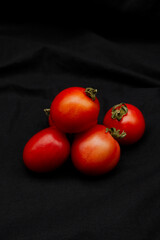 Tomato placed on black fabric background. Red tomatoes texture with the concept of fresh vegetable, organic and healthy product. Close-up a group of tomatoes with copy space. Still life food photo.