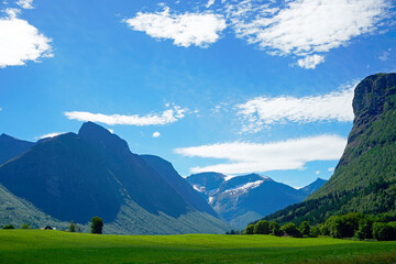 Mountains and nature of Norway. Summer and sunny day. Green valley and white clouds. Blue sky. Snow...