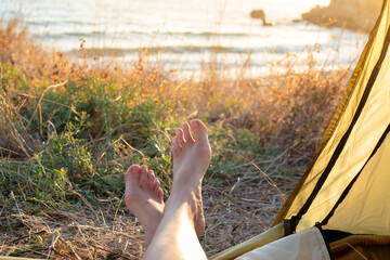 tourist tent with protruding female legs on the seashore at dawn. Camping. Travel and tourism