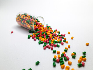 Colorful mixed masterbatch granules spilling from a glass tube on a white background.Color pigment carrier polymers in the plastics industry