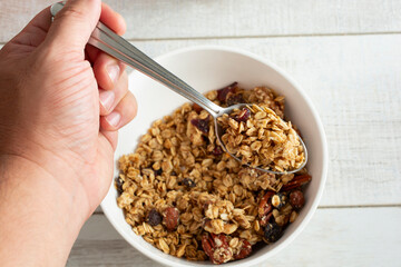 A top down view of a hand holding a spoonful of granola cereal.