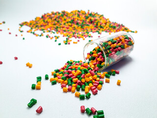 Colorful mixed masterbatch granules spilling from a glass tube on a white background.Color pigment carrier polymers in the plastics industry