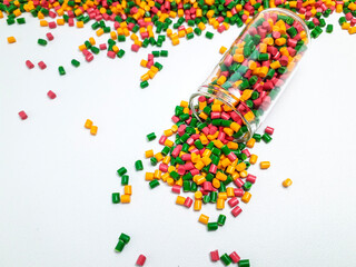 Colorful mixed masterbatch granules spilling from a glass tube on a white background.Color pigment...