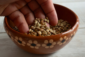 A closeup view of a hand digging into a bowl of raw green lentils.