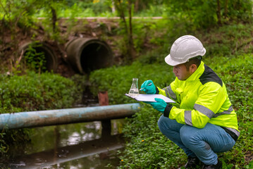 An ecologist in a green jacket sitting aside the pond try to  examination the quality of water  in...