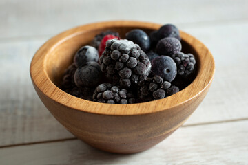A closeup view of a small wood bowl of frosted berries.