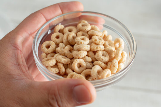 A view of a hand holding a small glass bowl of toasted o's creal.