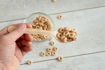 A view of a hand holding a spoon of toasted o's oat cereal.