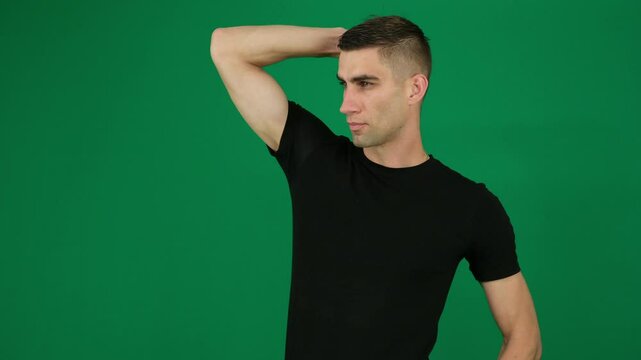man straightens the hair on his arm, beautiful muscles. emotions of a handsome man guy on a green background chromakey close-up dark hair. young man
