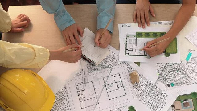 Architect and safety engineer discussion about building construction use blueprint on table with architectural document, measurement tool and wooden block scatter around at modern office. Delineation.