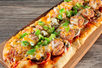 A view of a flatbread, featuring toppings as bell pepper, sausage and cheese.