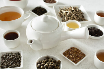 A view of a white teapot surrounded by a variety of loose leaf tea.