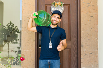 Happy delivery man with a water jug on his shoulder giving a thumbs up gesture