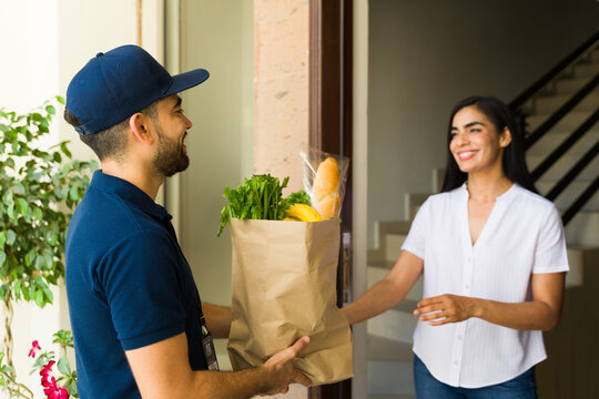 Attractive delivery guy handing a bag of groceries to a woman at her doorstep