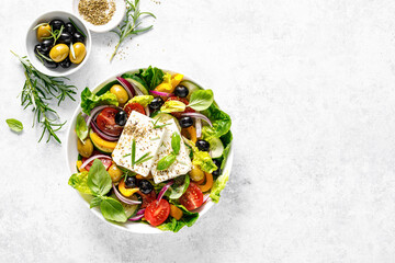 Fresh healthy vegetable Mediterranean food salad of Greek feta cheese, tomato, olives, pepper, lettuce and green basil leaves, top view