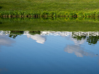 A Virginia neighborhood pond mirrors the sky, clouds, and a white fence in its tranquil waters.