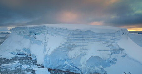 Antarctica giant blue glacier under dramatic evening sunset sky. Snow covered ice wall formation...