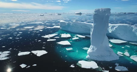 Selbstklebende Fototapeten Gletscher Towering melting iceberg in Arctic icy ocean. Snow covered glacier drift under blue sunny sky. Pure ice floats in turquoise water. Ecology, melting ice, climate change global warming. Aerial view  © mozgova