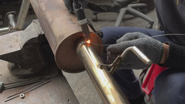 Welding stainless steel pipes with a tig welder.Pipe welding using a special machine.Weld stainless steel pipe and add stainless steel wire to the workpiece.Car pipe welding.Close up shot.