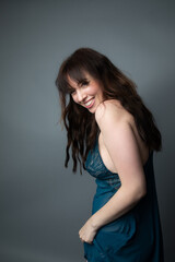 Fototapeta premium Studio portrait of a beautiful caucasian woman wearing a royal blue nightgown. She has long wavy brown hair. She is laughing and looking over her shoulder. The background is grey.
