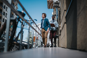 Fototapeta premium A Caucasian and an African American businessman walking together between modern buildings, engaging in a serious conversation about business.