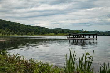 Photo of Otsego Lake captured by the marina in Cooperstown. There is a wooden dock in the lack with a roof.