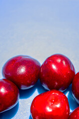 A bunch of red cherries are arranged in a circle on a blue background. The cherries are shiny and ripe, and they seem to be the main focus of the image
