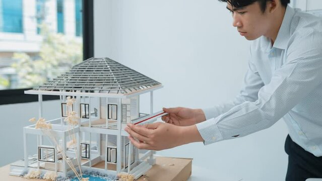 Close up of professional male architect engineer measure house model and using laptop analysis data at meeting table with house model and map . scatter around. Focus on hand. Immaculate.