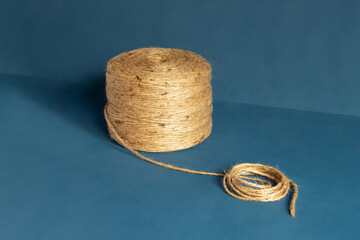 Close-up of a large spool of natural jute twine against a blue background, ideal for crafting, packaging, and gardening projects.