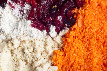 A close-up view of four distinct ingredients side by side: oat flour, ground almond, chopped plum, and grated carrot. The vivid colors and varied textures make this image visually appealing. Fodd.