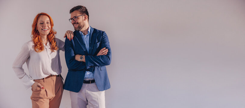 Business partners posing in front of gray background, looking at camera and smiling.